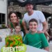 Family of four posing with a birthday cake that reads "BREXTON" in front of a building with a stone archway.