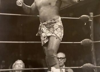 Wrestler Siva Afi in the ring, wearing a patterned sarong and a headband, giving two thumbs up.