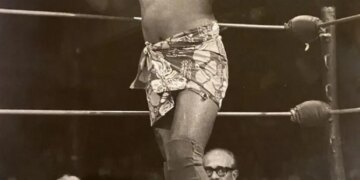 Wrestler Siva Afi in the ring, wearing a patterned sarong and a headband, giving two thumbs up.