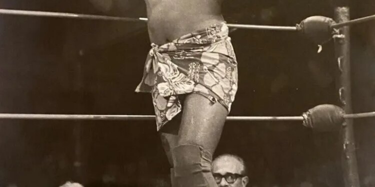 Wrestler Siva Afi in the ring, wearing a patterned sarong and a headband, giving two thumbs up.