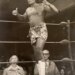 Wrestler Siva Afi in the ring, wearing a patterned sarong and a headband, giving two thumbs up.