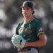 A male baseball player in a green Kingsburg uniform with an American flag patch and a black cap with a green "K" on it, wearing a light blue glove.