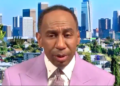 Stephen A. Smith in a lavender suit with a city skyline in the background.