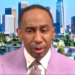 Stephen A. Smith in a lavender suit with a city skyline in the background.