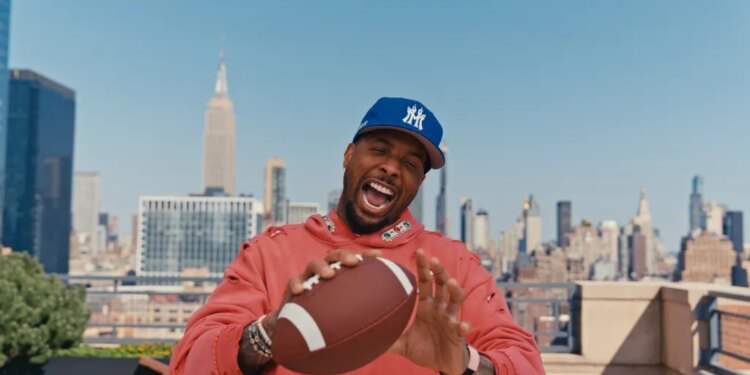 Odell Beckham Jr. smiling and holding a football on a New York City rooftop.
