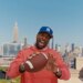 Odell Beckham Jr. smiling and holding a football on a New York City rooftop.