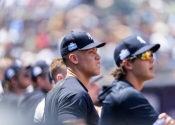 Aaron Judge in the dugout wearing a Yankees cap with a "Play Ball Weekend" patch.