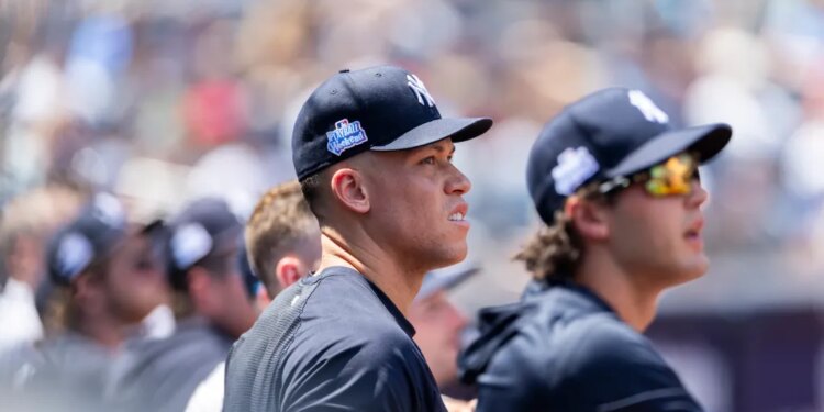 Aaron Judge in the dugout wearing a Yankees cap with a "Play Ball Weekend" patch.