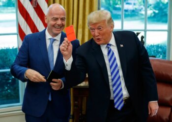 Donald Trump holding up a red card while Gianni Infantino smiles beside him.