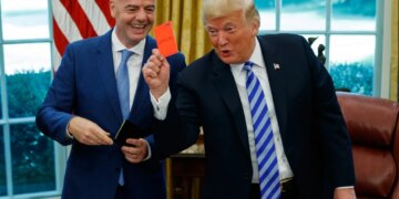 Donald Trump holding up a red card while Gianni Infantino smiles beside him.