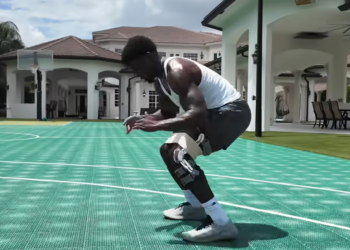 A man wearing a knee brace squats on a basketball court.