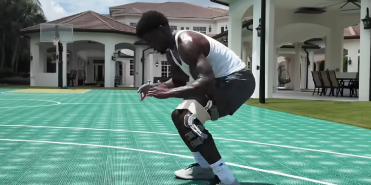A man wearing a knee brace squats on a basketball court.