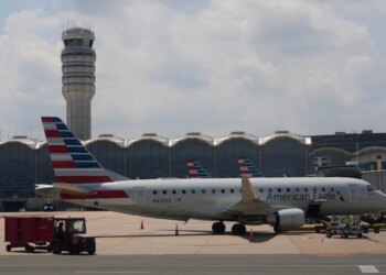 An American Eagle plane parked at a gate at Ronald Reagan Washington National Airport, with the air traffic control tower in the background.