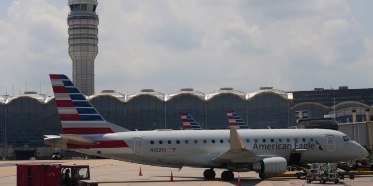 An American Eagle plane parked at a gate at Ronald Reagan Washington National Airport, with the air traffic control tower in the background.