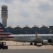 An American Eagle plane parked at a gate at Ronald Reagan Washington National Airport, with the air traffic control tower in the background.