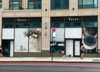 The exterior of Tatte Bakery & Cafe on the Upper East Side, featuring window displays of floral arrangements, a coffee, and a blueberry tart.