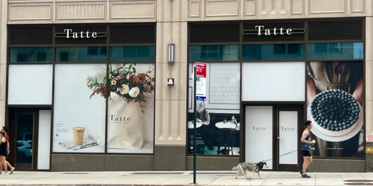 The exterior of Tatte Bakery & Cafe on the Upper East Side, featuring window displays of floral arrangements, a coffee, and a blueberry tart.