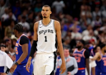 A basketball player in a white Spurs jersey with the number 1 stands on the court.