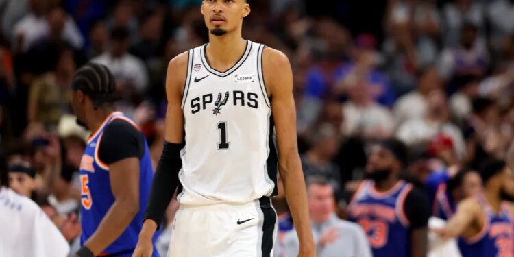 A basketball player in a white Spurs jersey with the number 1 stands on the court.